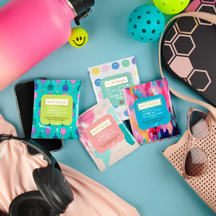 All Smiles print Well-Kept screen and lens wipes packs styled with sunglasses, a pink water bottle, headphones, and a phone on a teal background