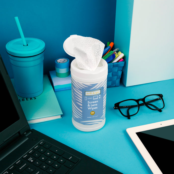 Blue wave print Well-Kept screen and lens wipes canister with a wipe pulled out, styled on a blue desk with a tumbler, glasses, and a laptop