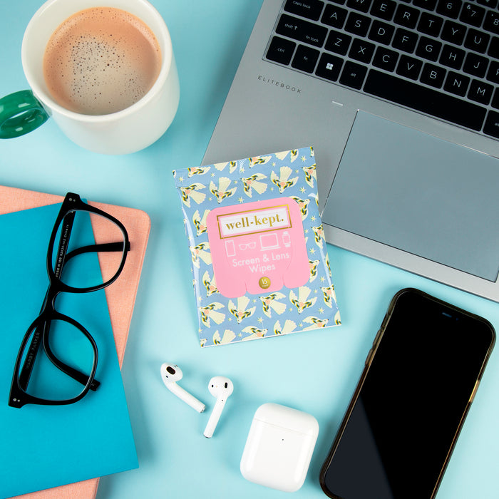 Floral print Well-Kept screen and lens wipes pack styled on a desk with coffee, a laptop, glasses, AirPods, and a phone